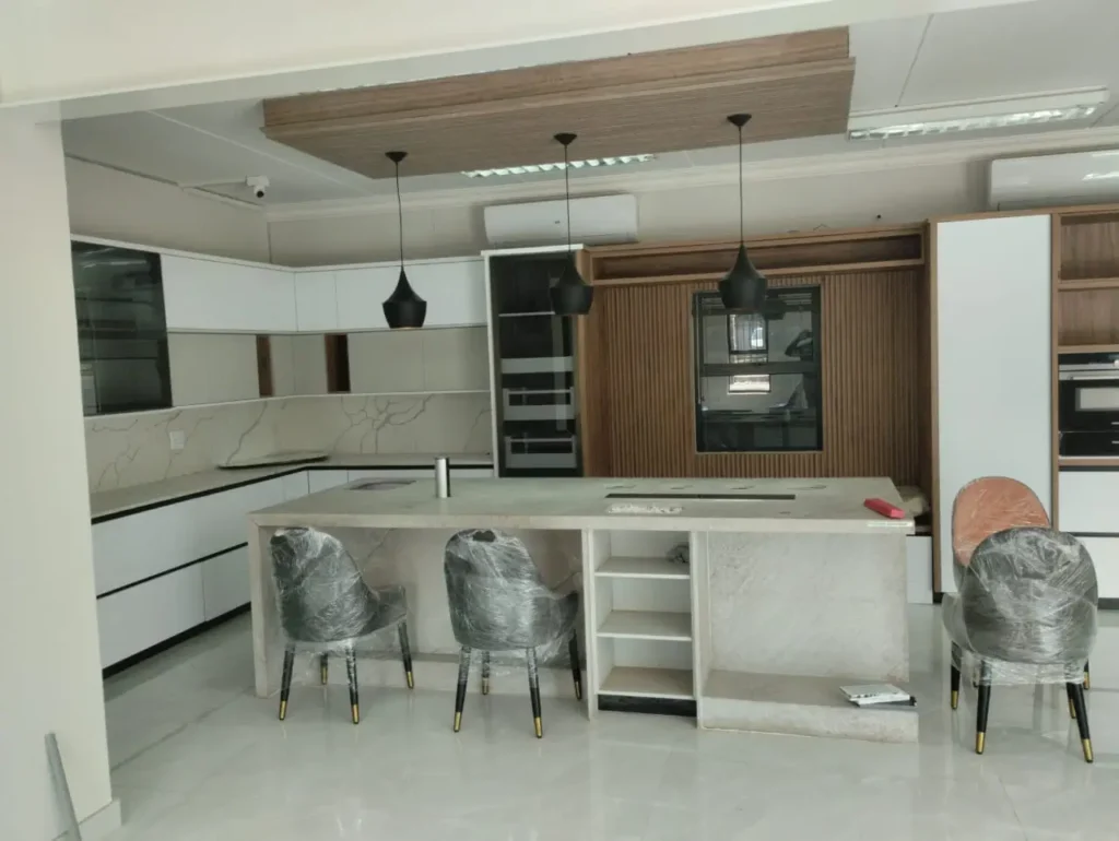 Large custom kitchen with a stone island, built-in cupboards, integrated appliances, and modern finishes, showing detailed carpentry and clean installation work
